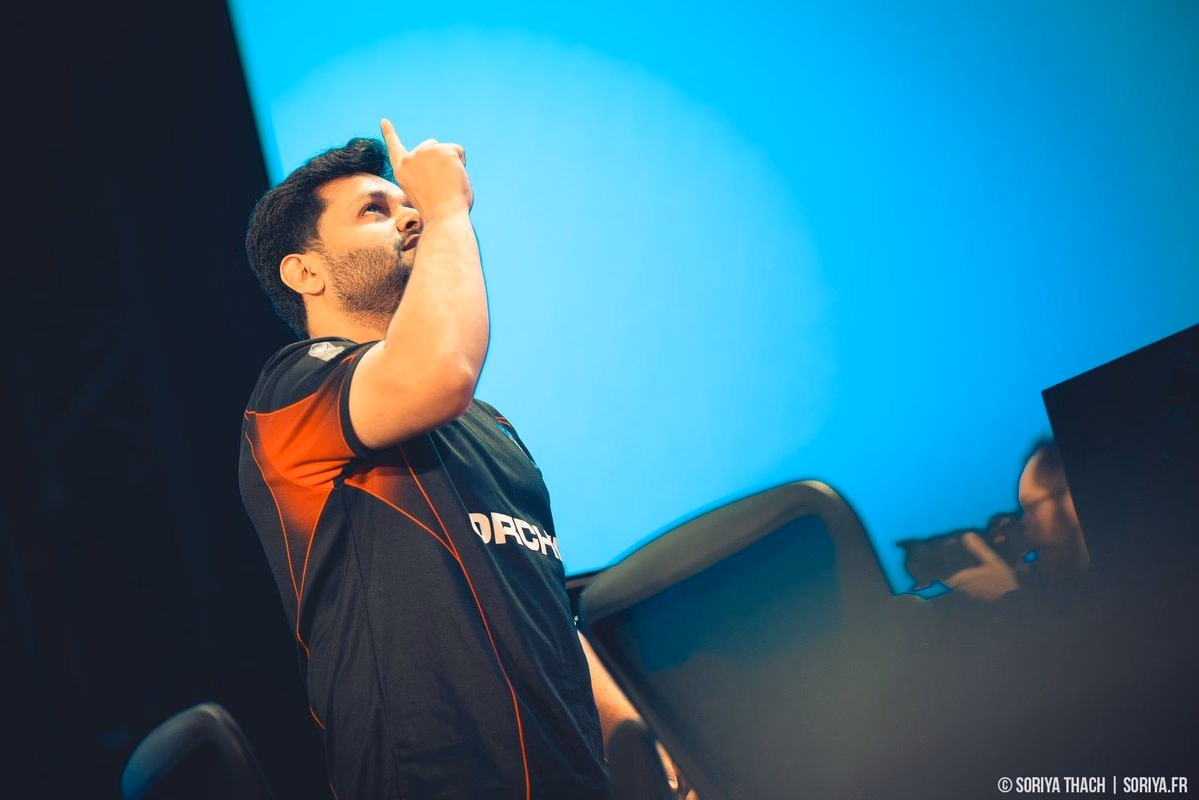 Dawood, in an Orchid jersey, points to the sky on stage in front of a blue screen.